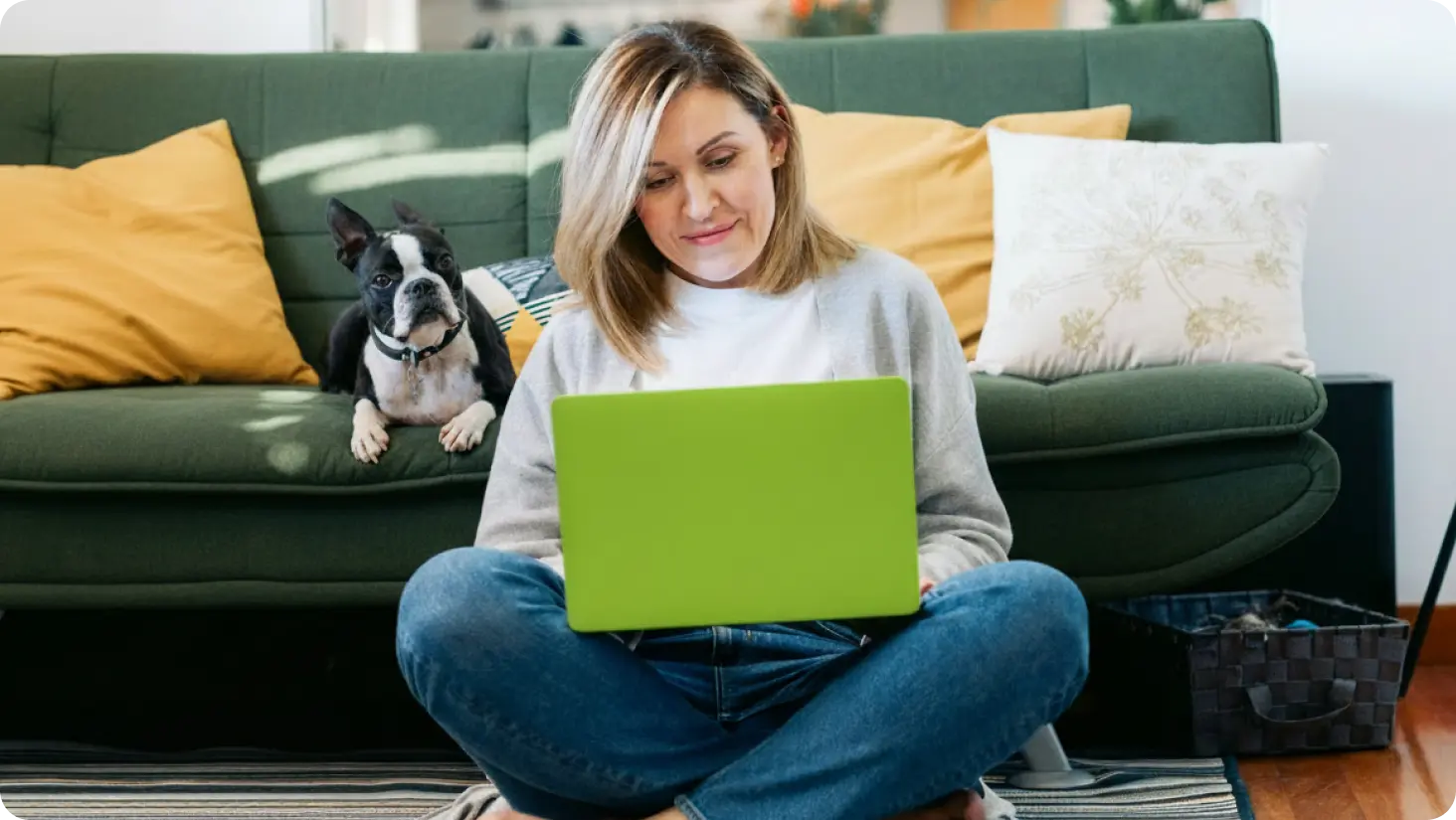 Smiling woman works on laptop PC with dog in background.