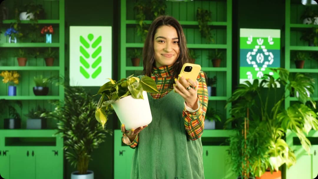 Smiling woman holding potted plant and smart phone.