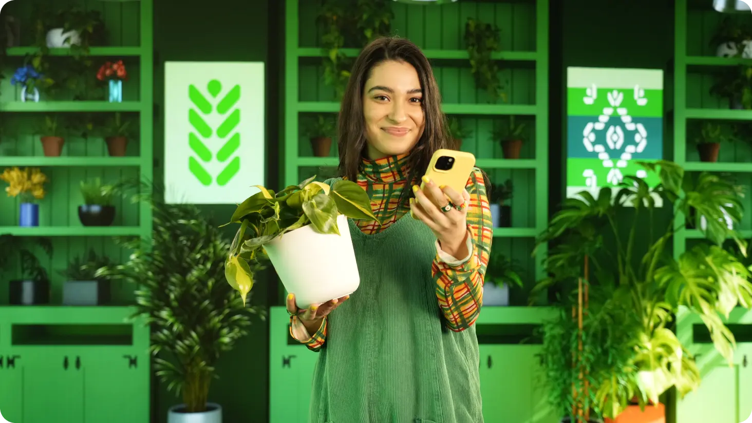 Smiling woman holding potted plant and smart phone.